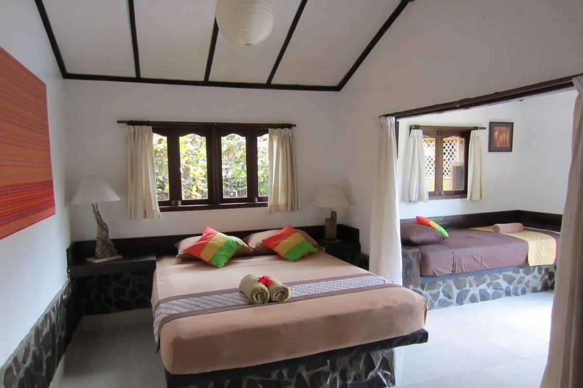 A bedroom with a large bed, a nightstand, a lamp, and a window with curtains.