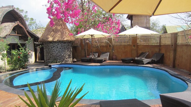 A swimming pool with lounge chairs and umbrellas, surrounded by a wooden deck and stone walls. - Gili Hideaway (Gili Trawangan)