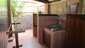 A bathroom with a stone wall, a wooden door, and a sink with a basin. - Gili Hideaway (Gili Trawangan)