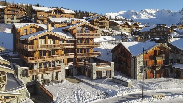 Un pueblo cubierto de nieve con edificios de madera, balcones y una vista despejada de las montañas al fondo.
