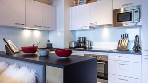 Una cocina moderna con armarios blancos, encimera negra, microondas de acero inoxidable y cafetera.
