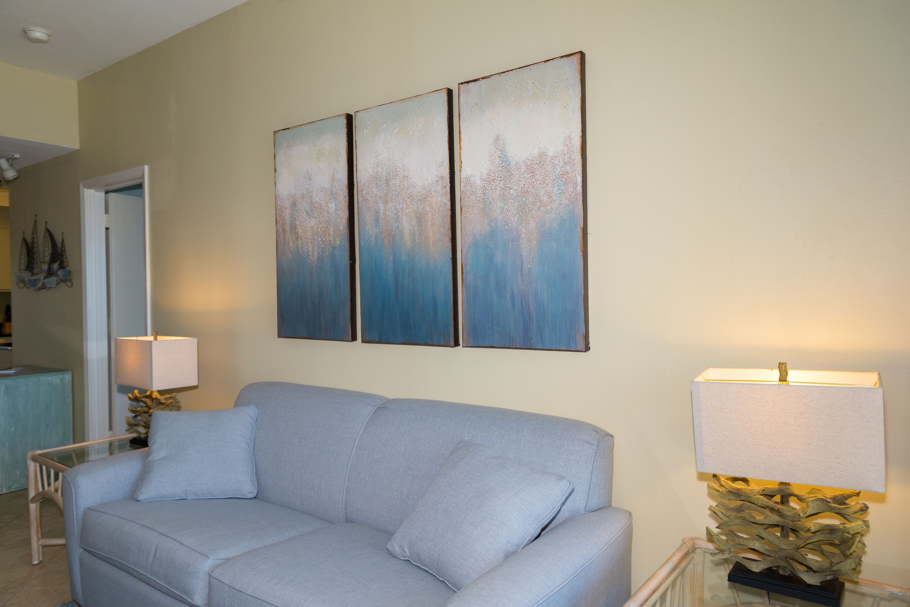 Een woonkamer met een lichtblauwe bank, een glazen salontafel en een wandlamp.
