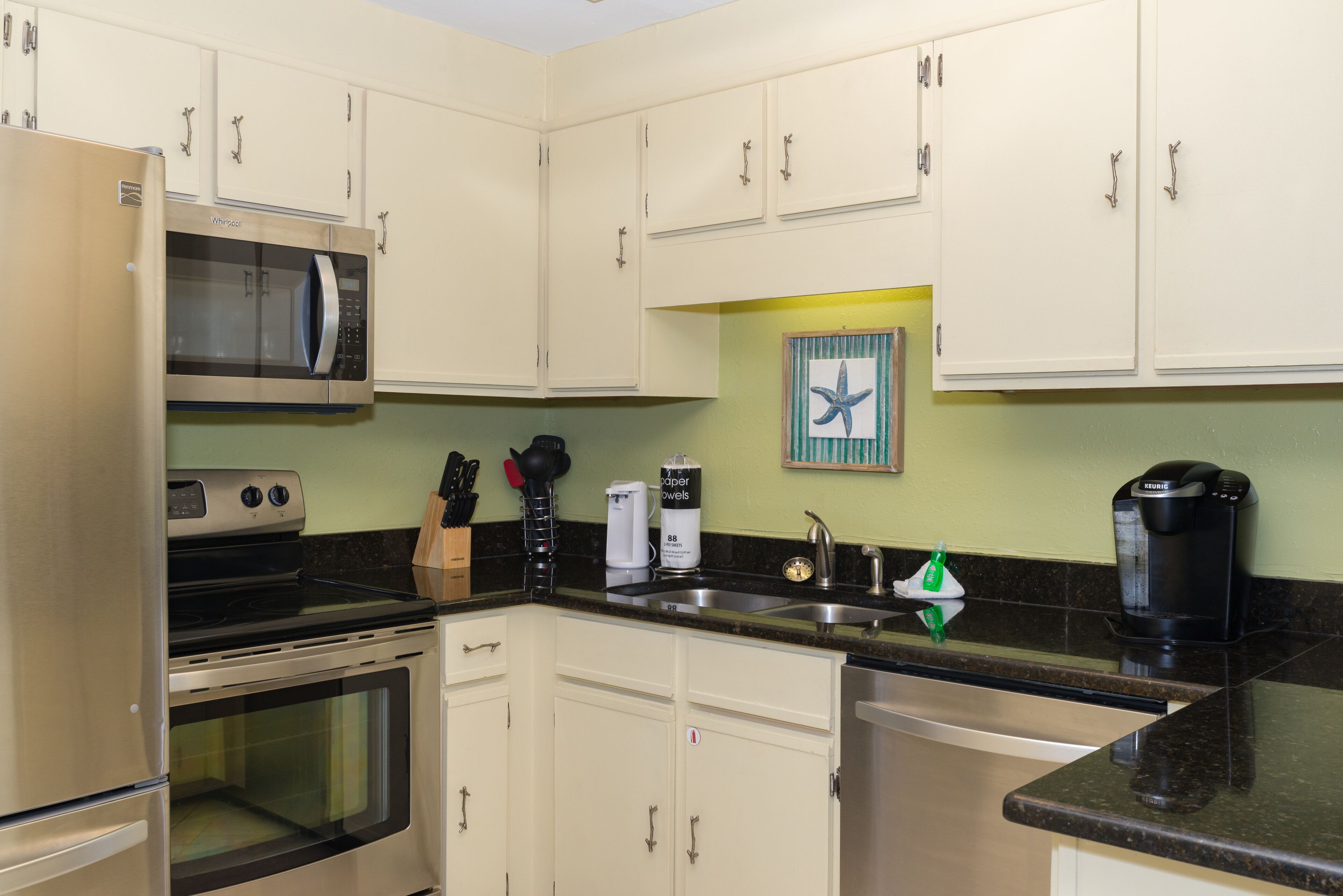 A kitchen with white cabinets, a stainless steel refrigerator, a microwave, a stove, a sink, and a coffee maker.