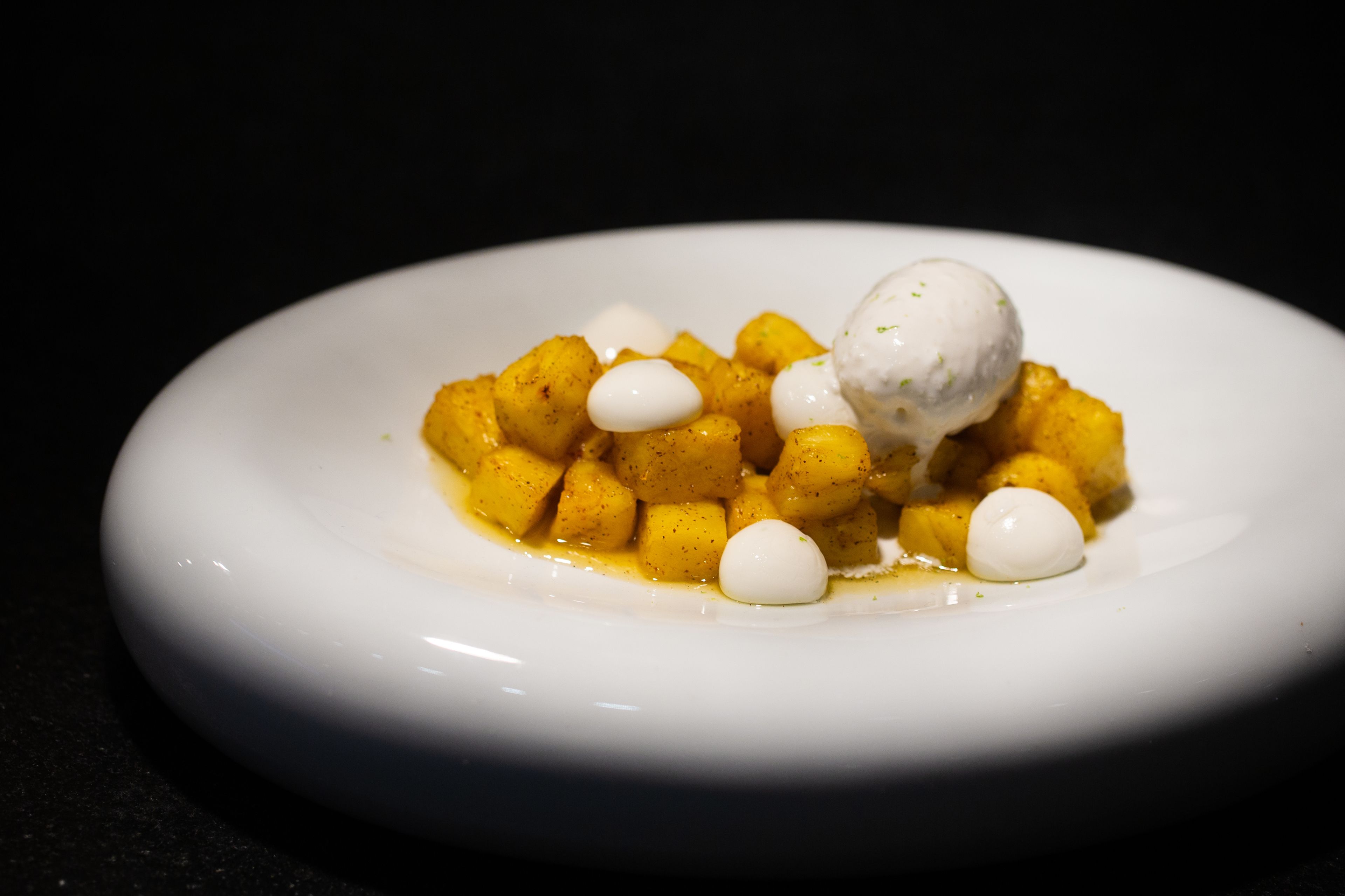 Plato blanco con un postre de cubos de comida amarilla y una porción de helado blanco.