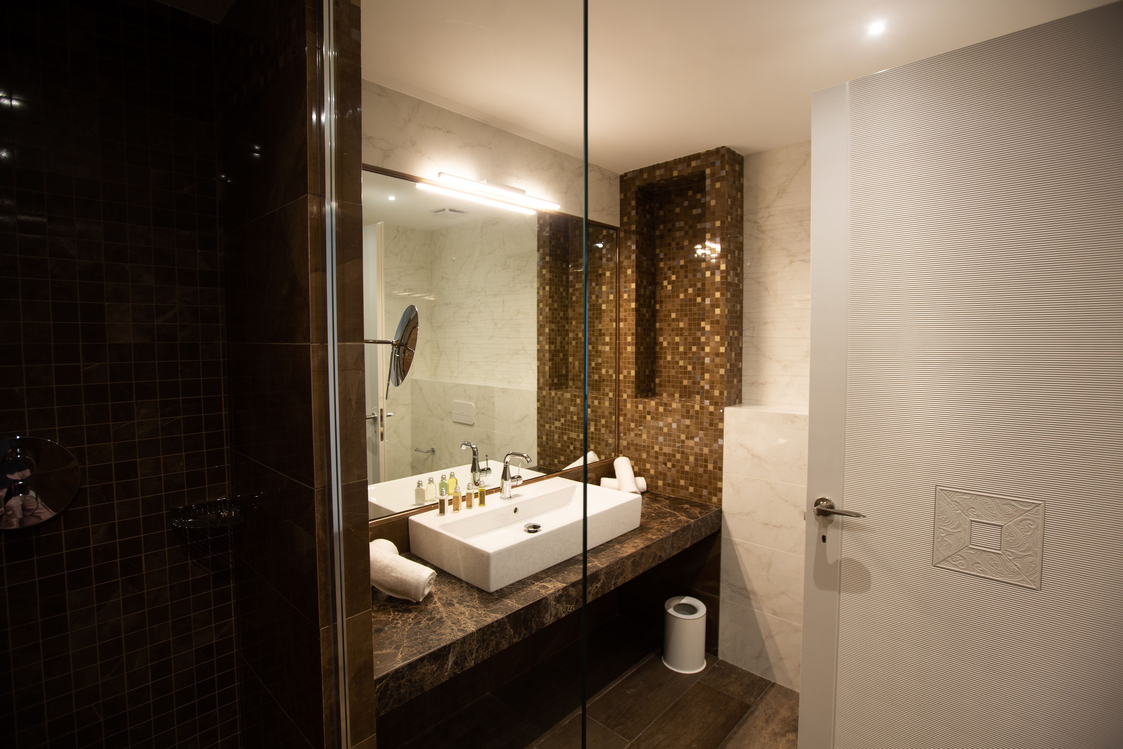 A modern bathroom with a glass shower enclosure, a white sink with a mirror, and a tiled wall.