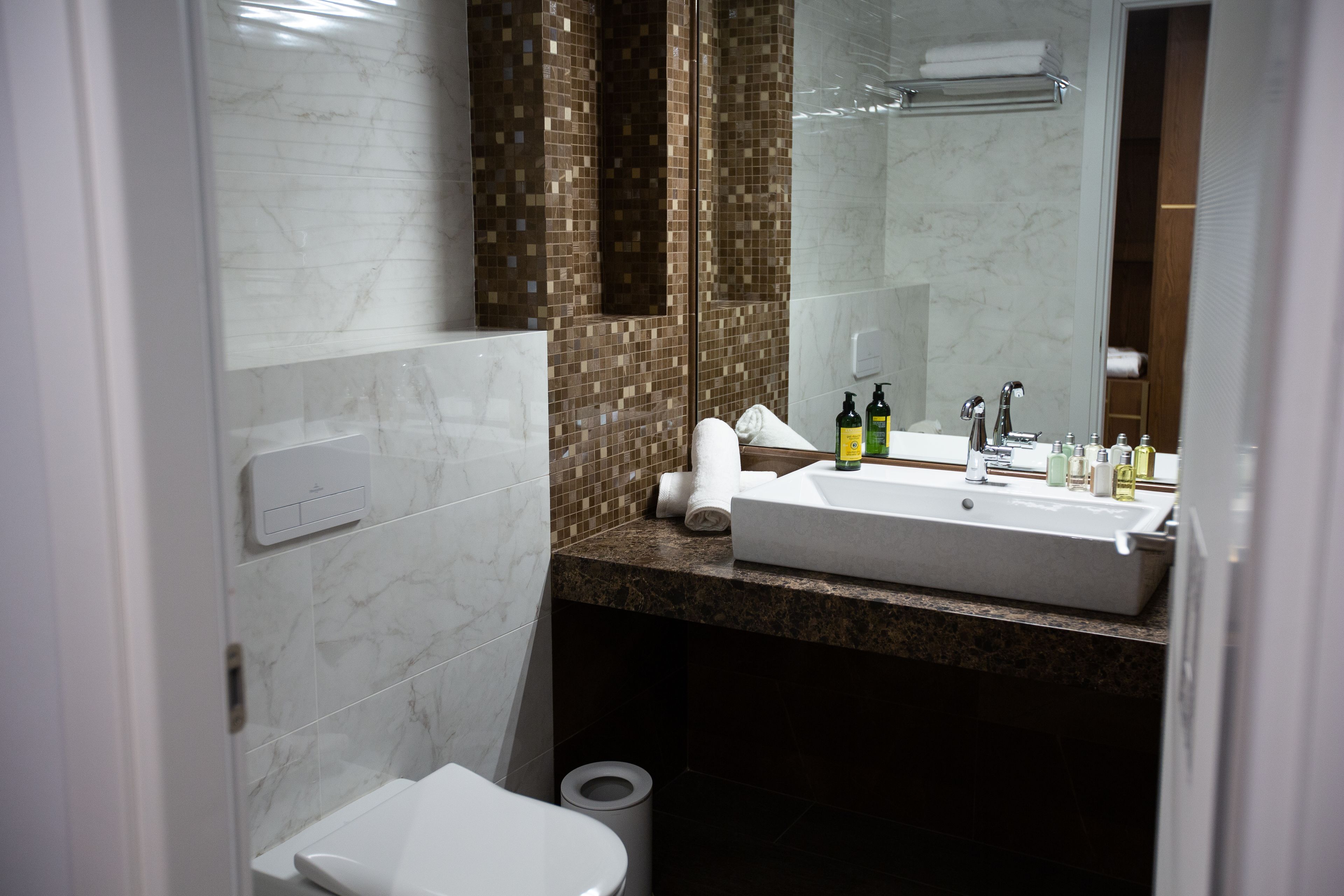 Une salle de bain moderne avec des toilettes blanches, un grand lavabo surmonté d’un miroir et un espace douche.