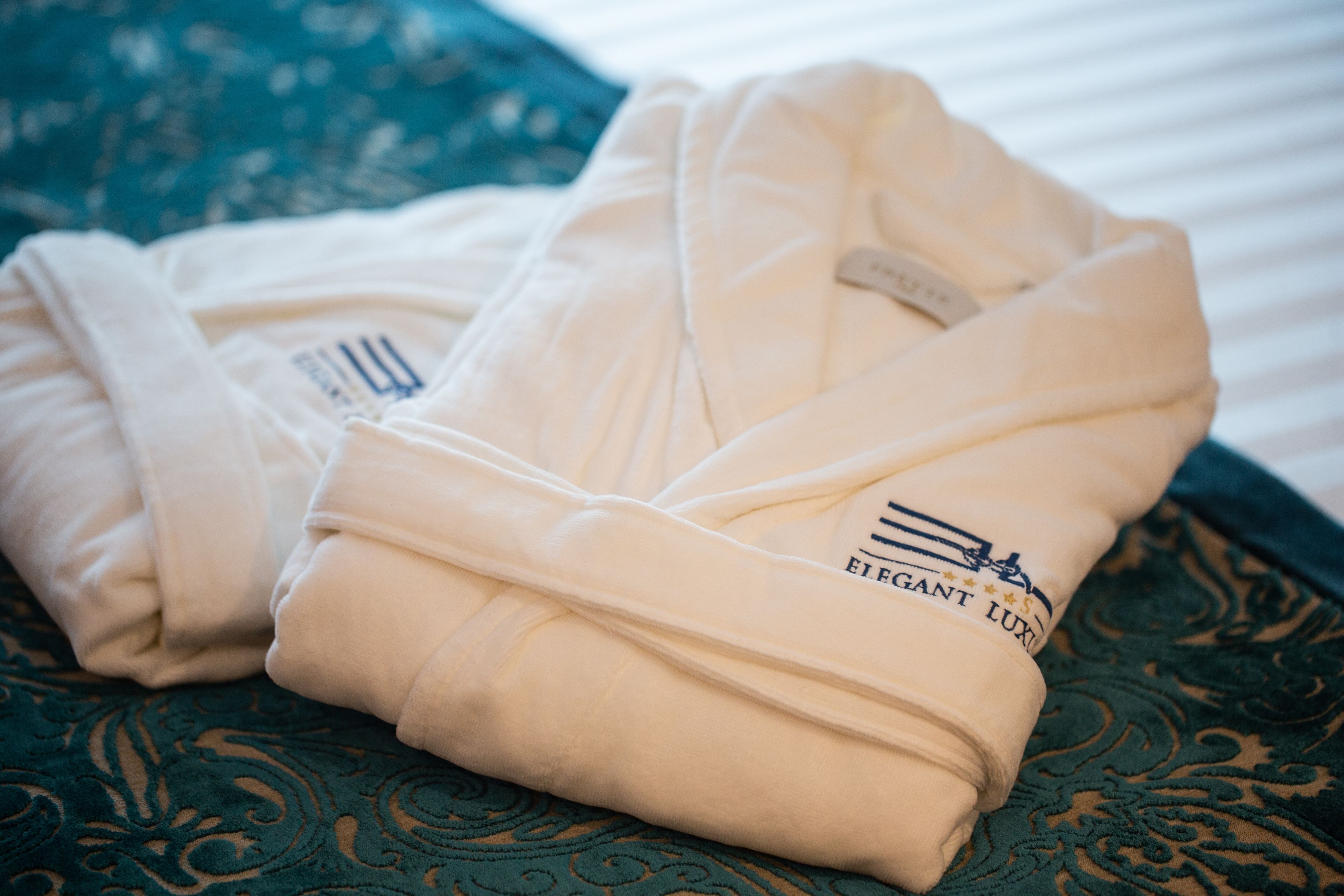 Two folded robes with a logo on them, placed on a patterned fabric.