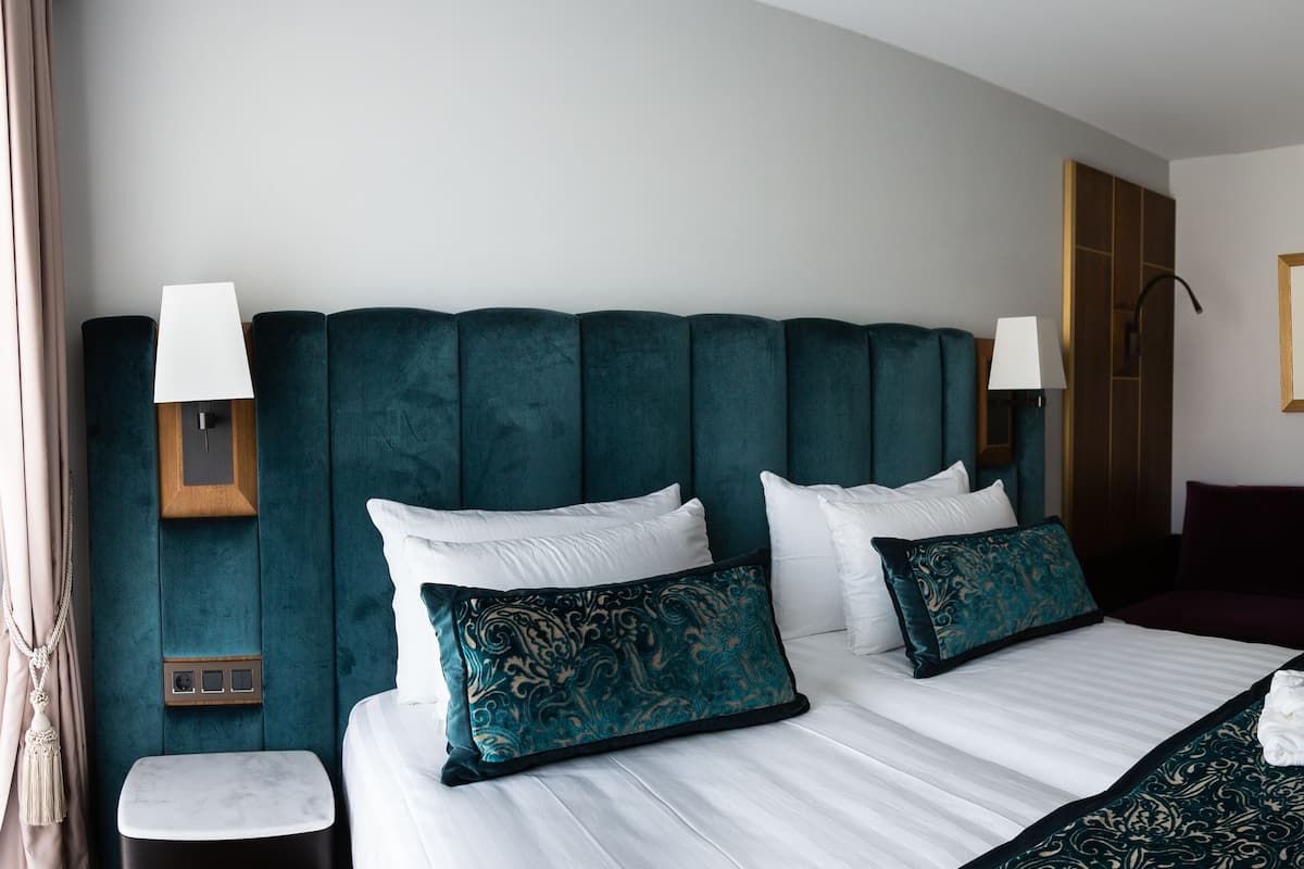 Habitación de hotel con una cama grande, una mesita de noche, un tocador, un aparador, un espejo y un cuadro en la pared.