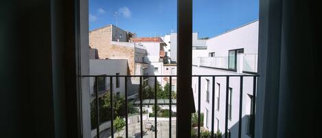 A courtyard with a view of buildings, a metal railing, and potted plants.