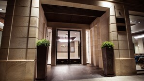 Una entrada de edificio moderna con una puerta oscura, grandes pilares de piedra y suelo de baldosas.