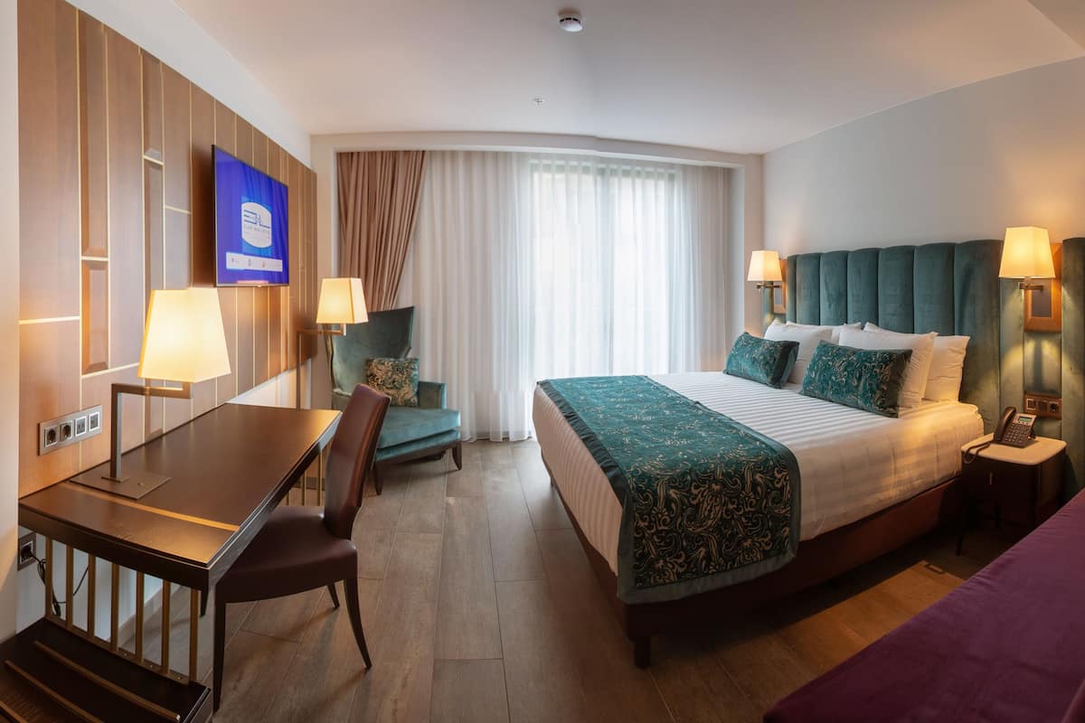 Habitación de hotel con una cama grande, un escritorio, una silla, una mesita y un sofá.
