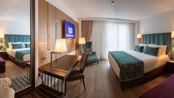 A hotel room with a large bed, a desk, a chair, a small table, and a sofa.