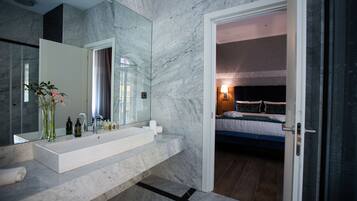 Un baño moderno con un espejo grande, lavabo blanco y paredes de mármol.