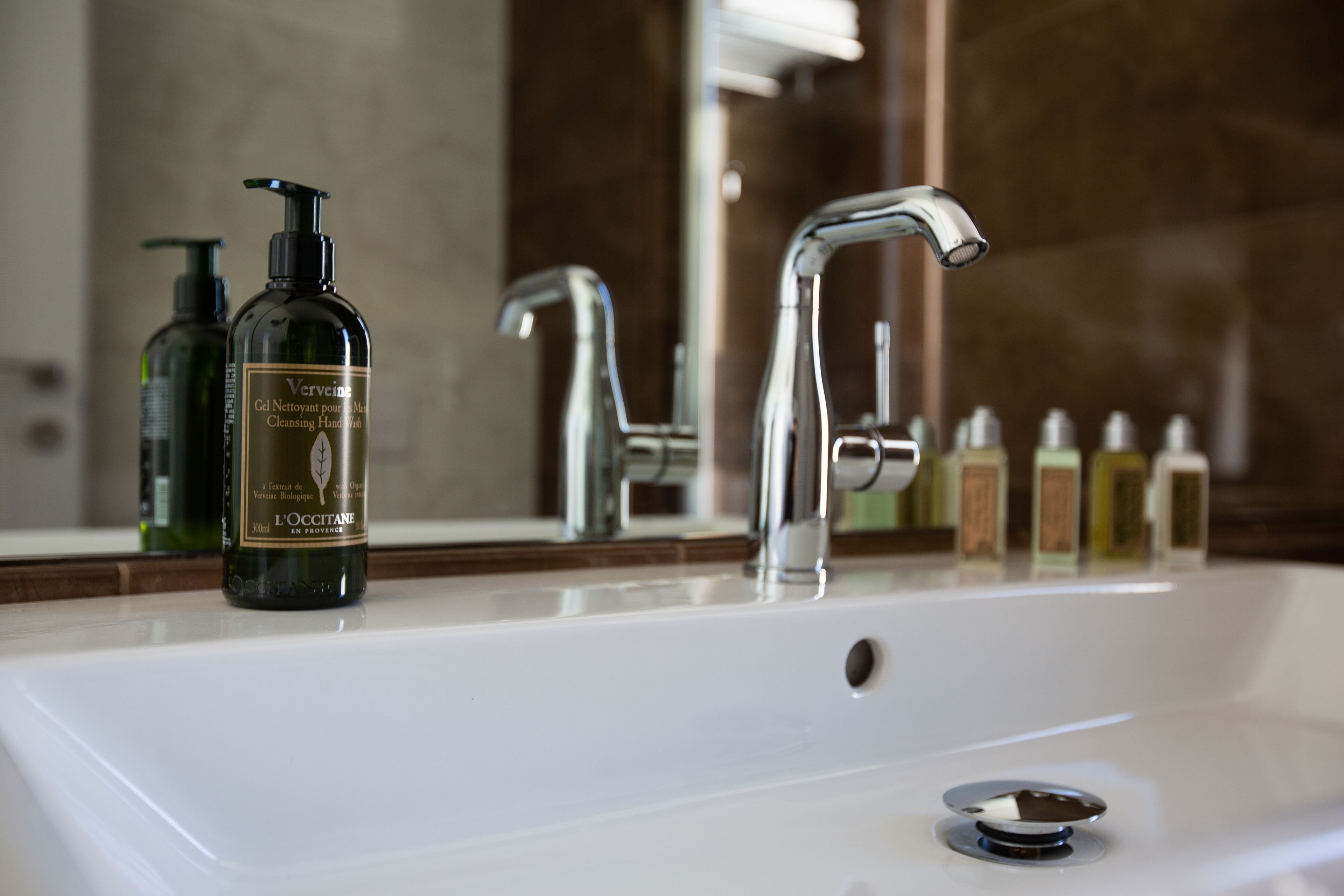 Un lavabo de salle de bain avec deux flacons de savon liquide pour les mains de la marque L'OCCITANE et un robinet chromé.