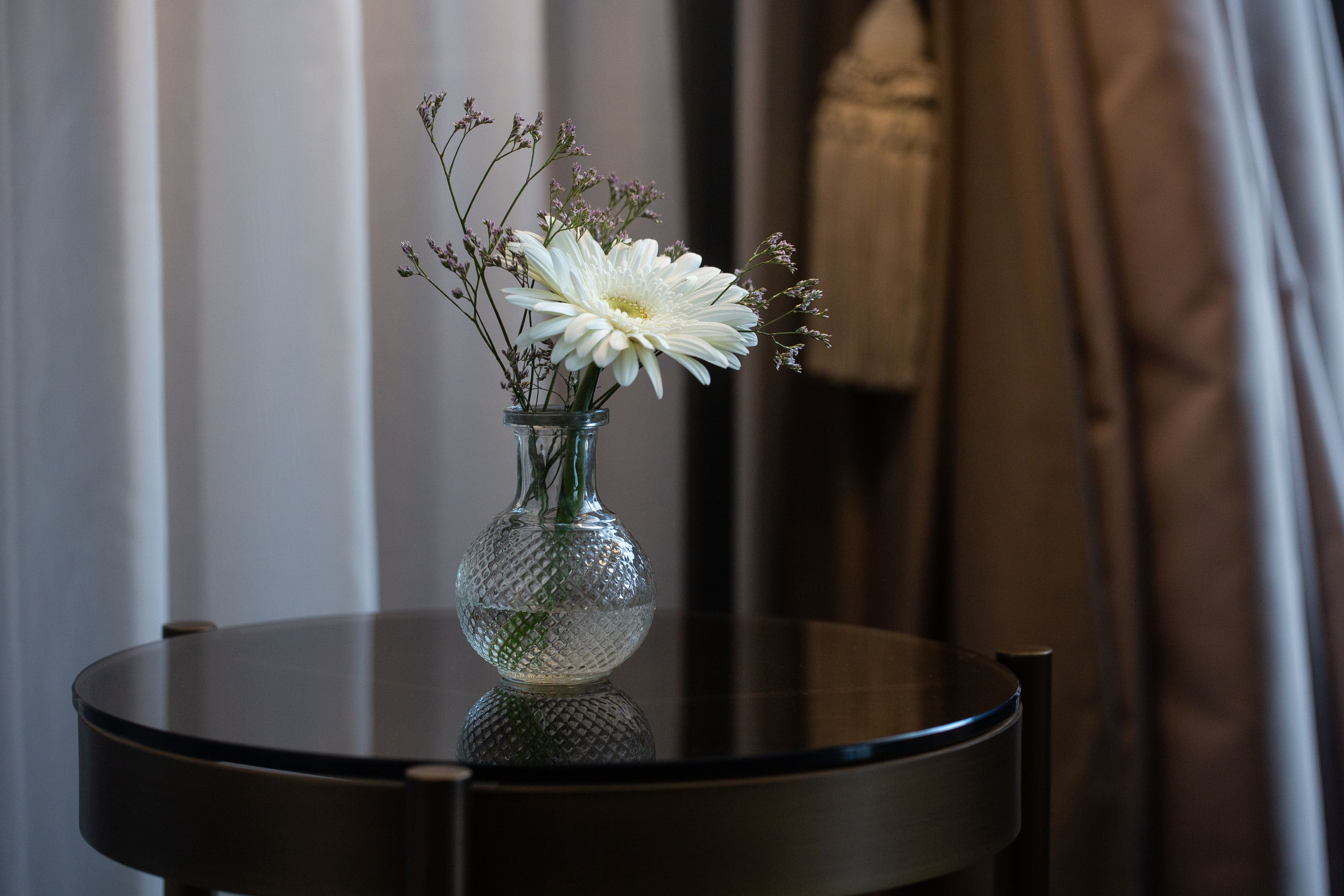 Una mesa redonda con un florero de cristal que contiene flores blancas y follaje.