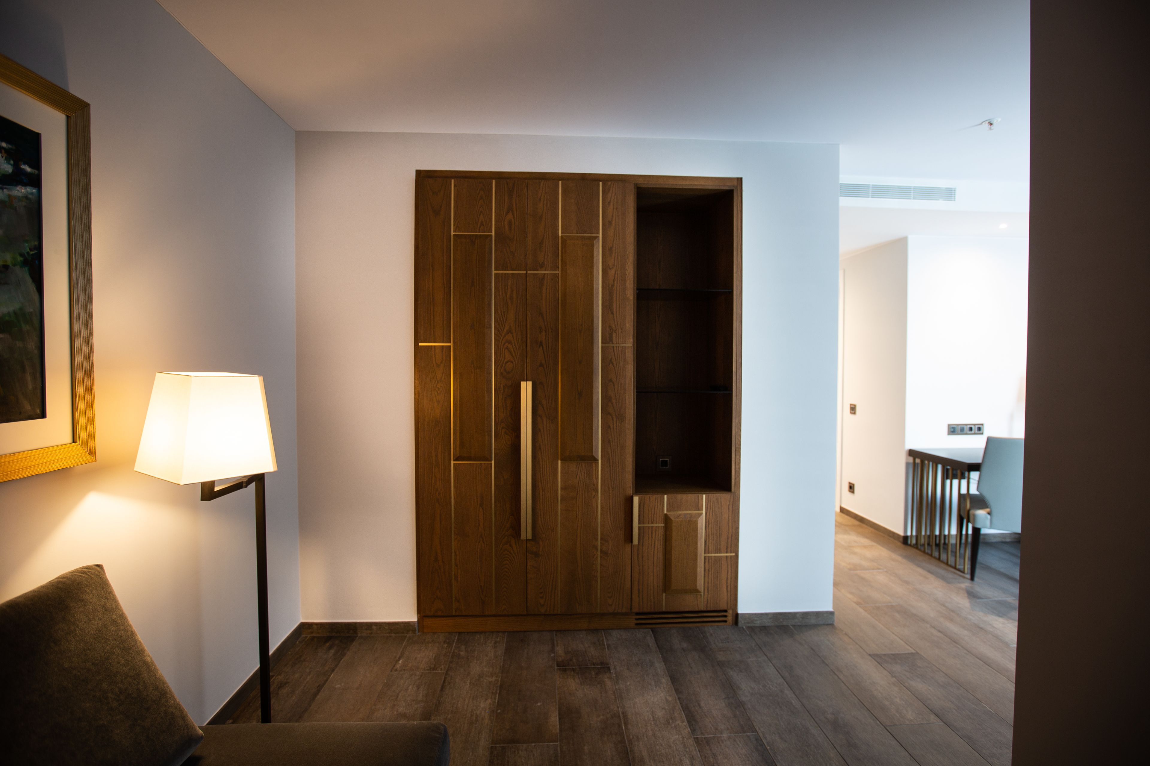 Une chambre moderne avec une armoire en bois, un lampadaire et un coin repas à l’arrière-plan.