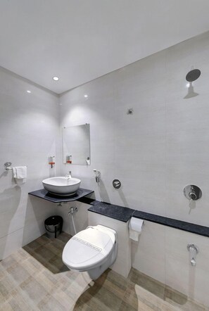 Uma casa de banho moderna com uma sanita branca, lavatório, chuveiro e espelho.
