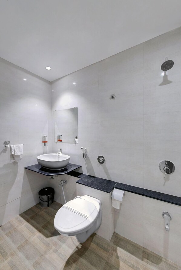 Un baño moderno con un lavamanos blanco, inodoro, cabezal de ducha y espejo.