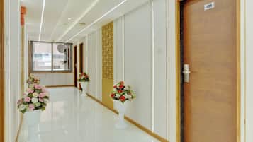 A hotel corridor with a wooden door labeled '106', a glass door with a view, and potted plants along the walkway.