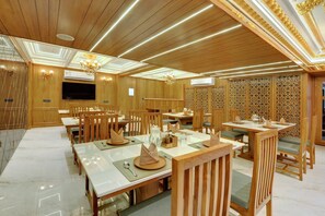 A dining area with wooden furniture, tables set with plates, and a chandelier. - Hotel Shital Inn (Ahmedabad)