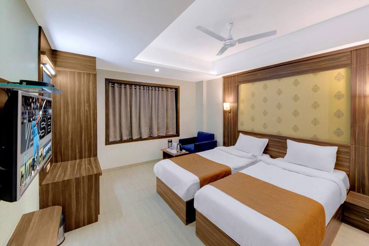 Une chambre d’hôtel avec deux lits, un ventilateur de plafond, une télévision, un bureau et une fenêtre avec des rideaux.