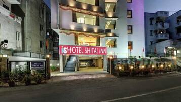 Um hotel chamado "Hotel Shital Inn", com uma placa grande, uma escadaria que leva à entrada e uma entrada com portão.