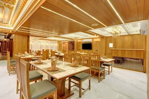 A spacious dining area with wooden tables and chairs, a chandelier, and a flat-screen TV mounted on the wall.
