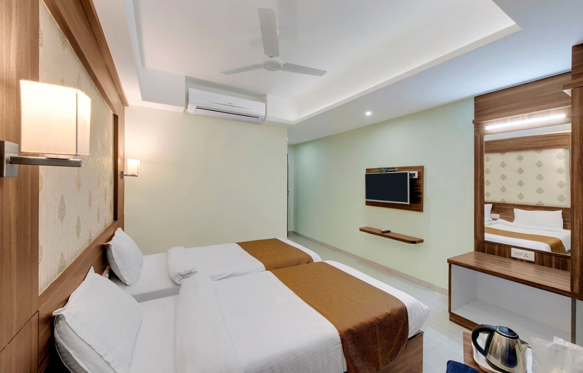 A hotel room with two beds, a ceiling fan, an air conditioning unit, a television, and a mirror.