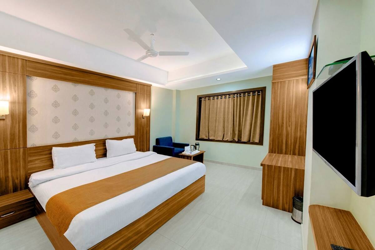 Une chambre d’hôtel avec un grand lit, un ventilateur de plafond, une télévision et une fenêtre avec des rideaux.