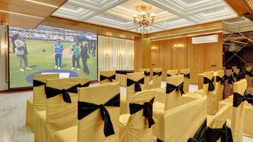 A conference room with rows of chairs, a large screen displaying a sports event, and a chandelier.