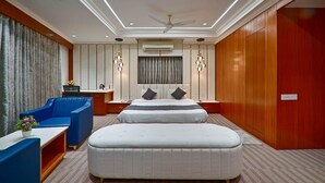 Quarto de hotel com uma cama grande, uma poltrona azul, uma escrivaninha pequena e um ventilador de teto.