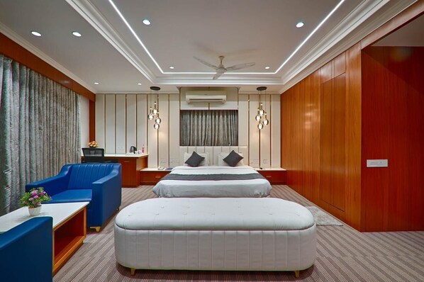 Quarto de hotel com uma cama grande, uma poltrona azul, uma escrivaninha pequena e um ventilador de teto.