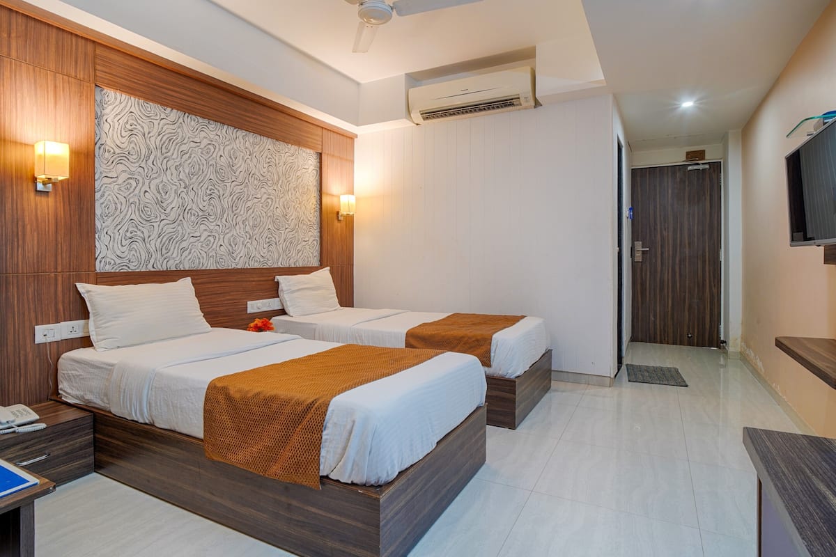 Une chambre d’hôtel avec deux lits, une tête de lit en bois, un climatiseur fixé au mur et un téléviseur mural.
