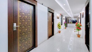 Corredor de hotel com porta de madeira com padrão decorativo, plantas em vasos e piso ladrilhado.
