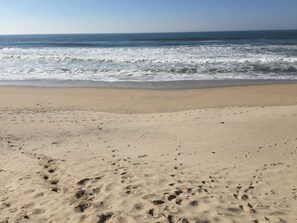 A beach with footprints in the sand and waves approaching the shore.