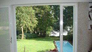 A room with a large sliding glass door leading to a backyard with a swimming pool, a grassy lawn, and a wooden deck.