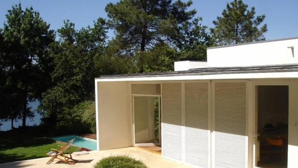 A modern house with a pool, a covered patio, and a view of trees.