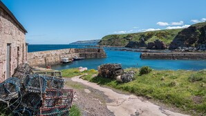 A coastal scene with a stone building, a harbor, and a clear blue sky.