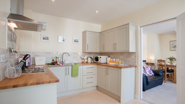 A modern kitchen with white cabinets, a wooden countertop, and a dining area with a blue sofa and table.