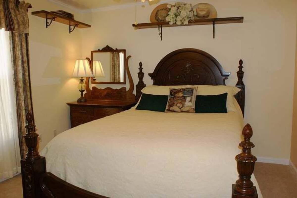 A traditional bedroom with a four-poster bed, a nightstand with a lamp, and a mirror above the bed.