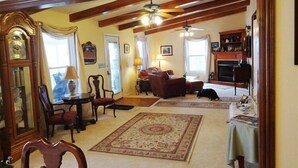A spacious living room with a fireplace, wooden beams, and a ceiling fan.