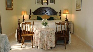 A bedroom with a large bed, two bedside lamps, a floral table, and a vase of flowers.