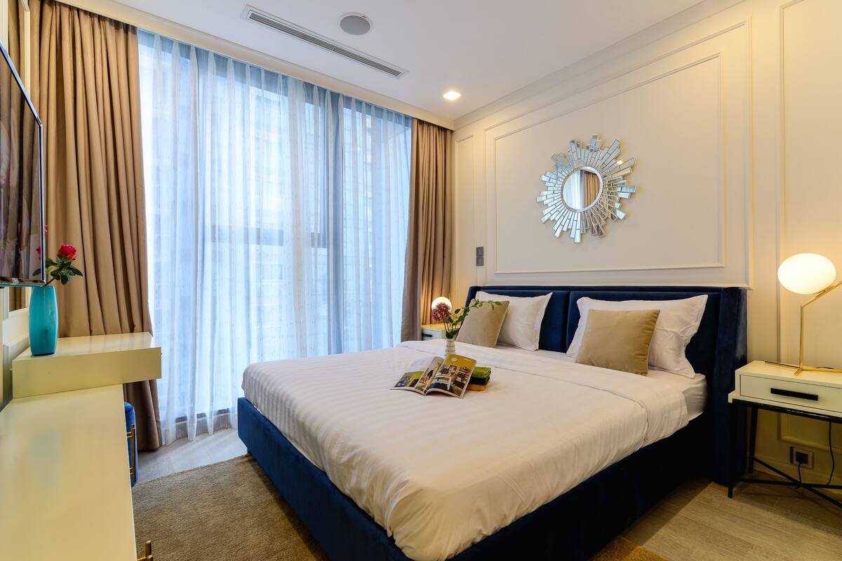 Une chambre d’hôtel avec un grand lit, une table de chevet, un miroir et une fenêtre avec des rideaux.