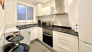 A compact kitchen with white cabinets, a built-in oven, a microwave, a coffee maker, and a window with frosted glass.