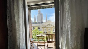 A balcony with a wooden table and chair, a potted plant, and a view of a cityscape with tall buildings.