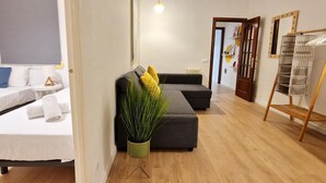 A modern hotel room with a sofa, a small table, a potted plant, and a wooden floor.