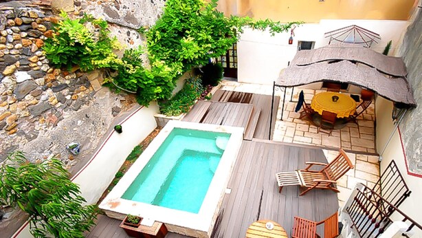 Un área de piscina en la azotea con terraza de madera, una piscina pequeña y mobiliario exterior.