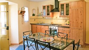 Una cocina con armarios de madera, una estufa a gas y una mesa de comedor de vidrio con sillas.