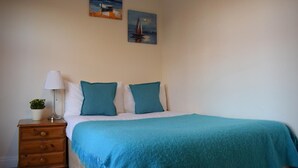 A bedroom with a bed, two pillows, a bedside table with a lamp, a small plant, and two wall-mounted paintings. - Magma Flat (London)