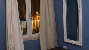 A room with a window, white curtains, a wooden dresser, and a mirror on the wall. - Il Borgo B&B (Corato)